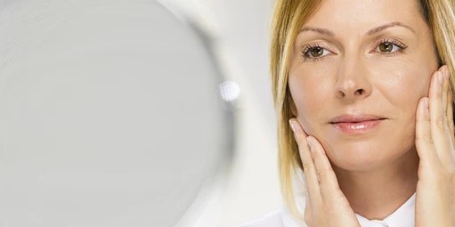 Woman who had eyelid surgery enjoys her reflection and rejuvenated appearance.